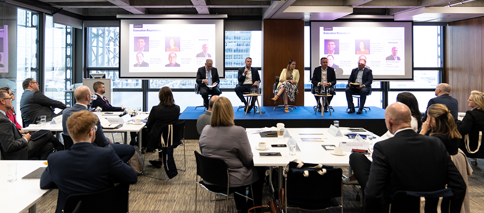 Panel of 5 people are on a stage facing the room
