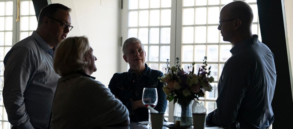 Four people are standing around a high table talking
